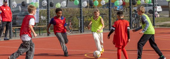 Kinder auf rotem Sportplatz spielen Fußball