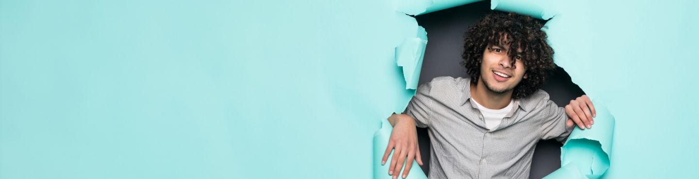 Junge mit krausem langem Haar schaut durch Papierwand