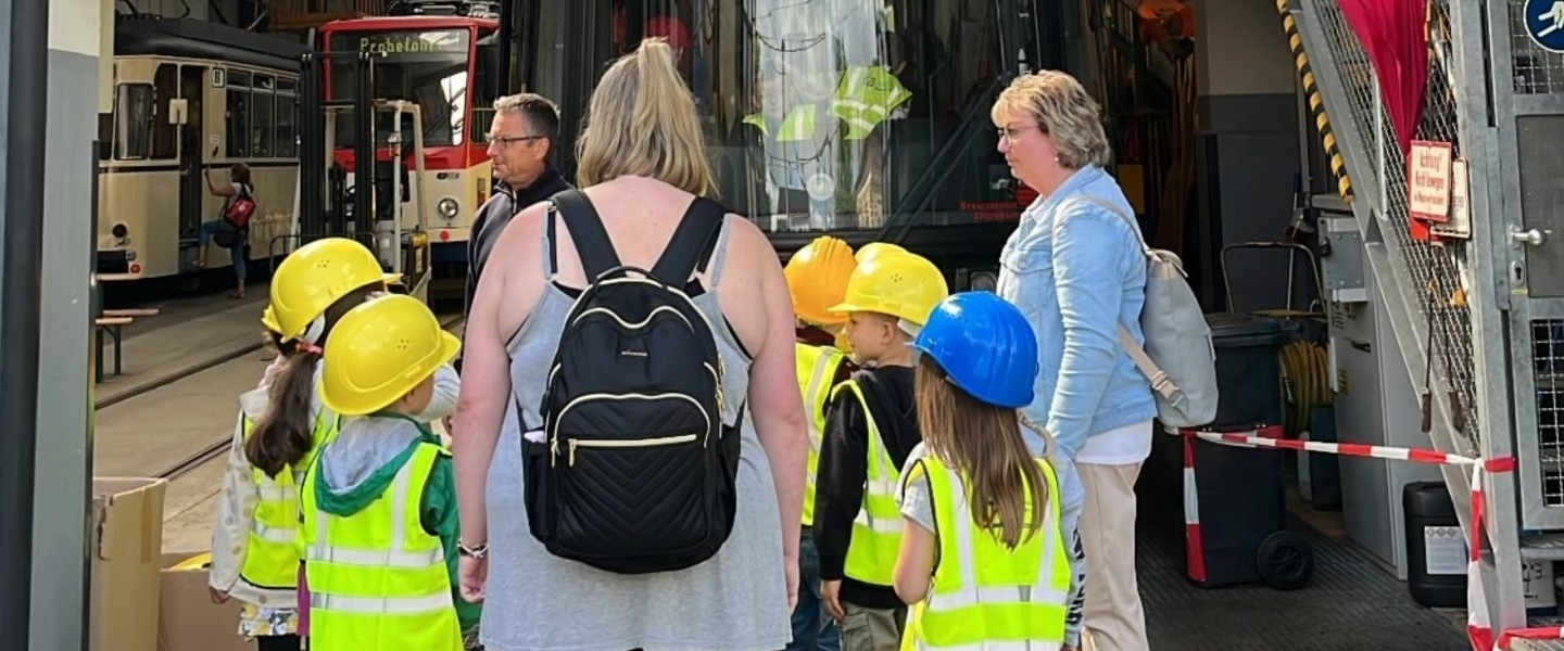 Kinder mit Schutzhelmen stehen mit Erziehern vor einer Bahn