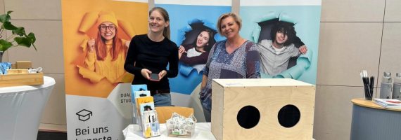 Zwei lächelnde Frauen an buntem Messestand