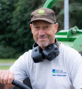 Mitarbeiter lächelt auf Rasenmäher in Kamera