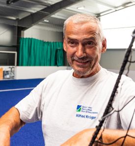 Mitarbeiter in Turnhalle stützt sich auf Netz und lächelt
