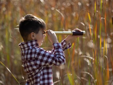 Ein Junge steht im Kornfeld und schaut durch ein Fernrohr